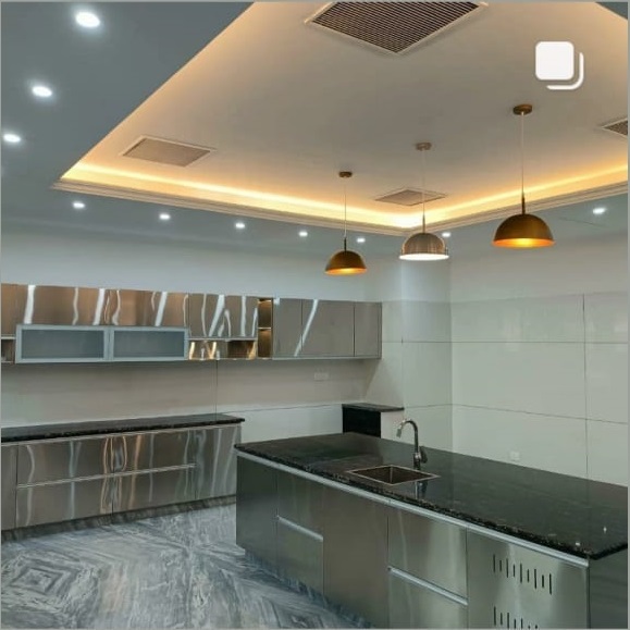 Modern kitchen featuring stainless steel cabinets, black countertop, and stylish pendant lights against a sleek, bright backdrop.