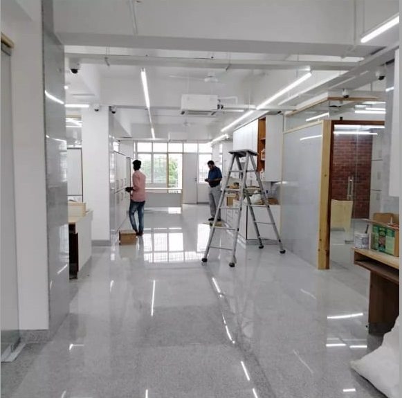 A bright, modern office space under renovation with two workers, a ladder, and polished floors, featuring large windows.